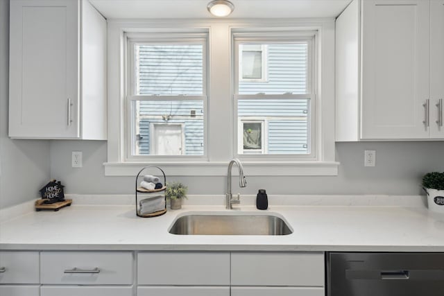 kitchen with dishwashing machine, white cabinets, light countertops, and a sink