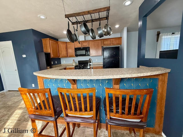 kitchen featuring light countertops, recessed lighting, brown cabinets, a kitchen breakfast bar, and black appliances