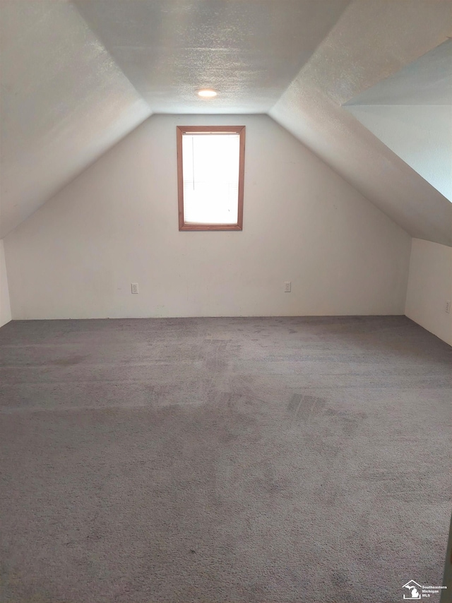 bonus room with lofted ceiling, carpet flooring, and a textured ceiling