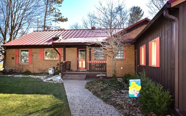 view of front of home featuring brick siding, a porch, metal roof, and a front lawn