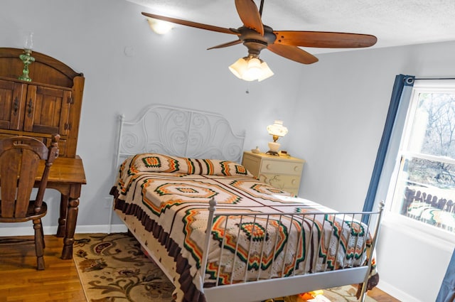 bedroom with ceiling fan, a textured ceiling, baseboards, and wood finished floors