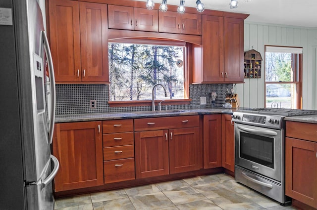 kitchen featuring tasteful backsplash, dark stone countertops, appliances with stainless steel finishes, brown cabinets, and a sink