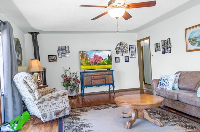 living area with a wood stove, ceiling fan, and wood finished floors