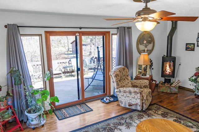 interior space with a healthy amount of sunlight, a wood stove, a ceiling fan, and wood finished floors