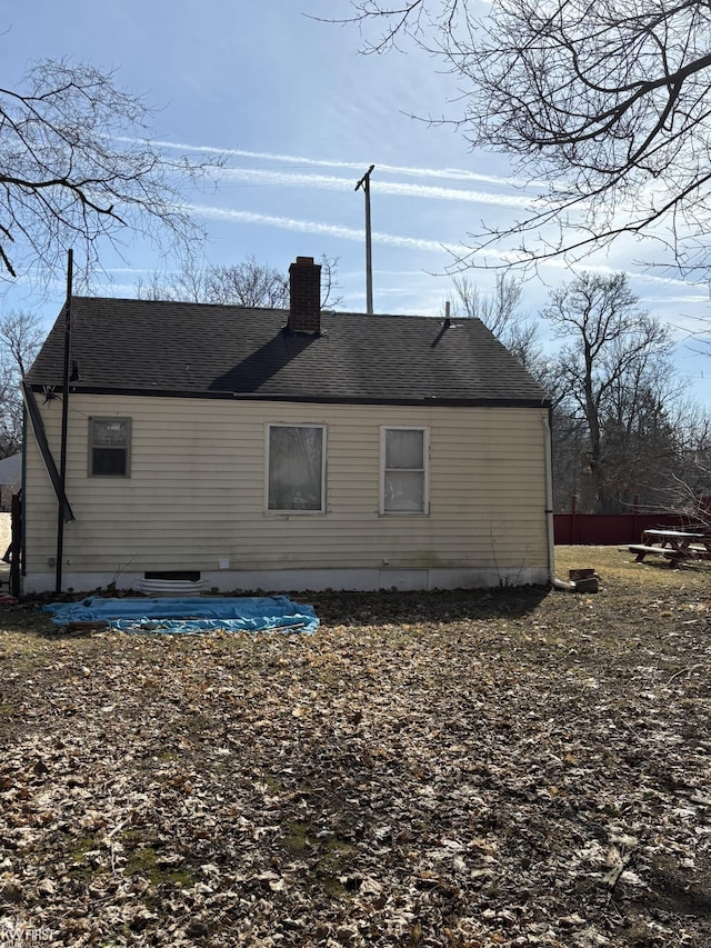 rear view of house with a chimney and roof with shingles