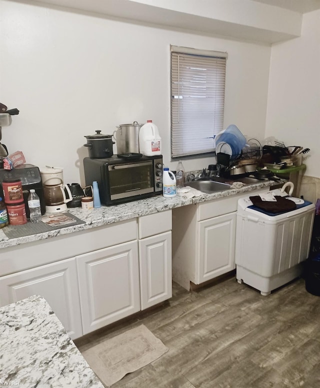 kitchen with a toaster, light countertops, wood finished floors, white cabinets, and a sink