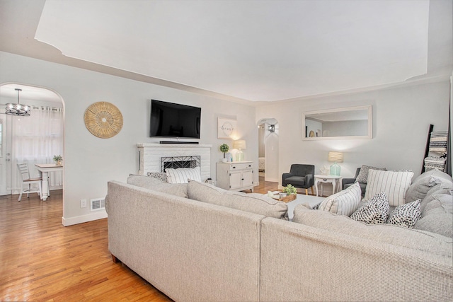 living area featuring visible vents, baseboards, light wood-type flooring, a fireplace, and arched walkways