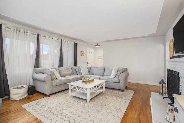 living area featuring baseboards, a fireplace with raised hearth, and hardwood / wood-style floors