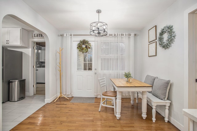 dining area featuring washer / clothes dryer, arched walkways, light wood-style floors, an inviting chandelier, and baseboards