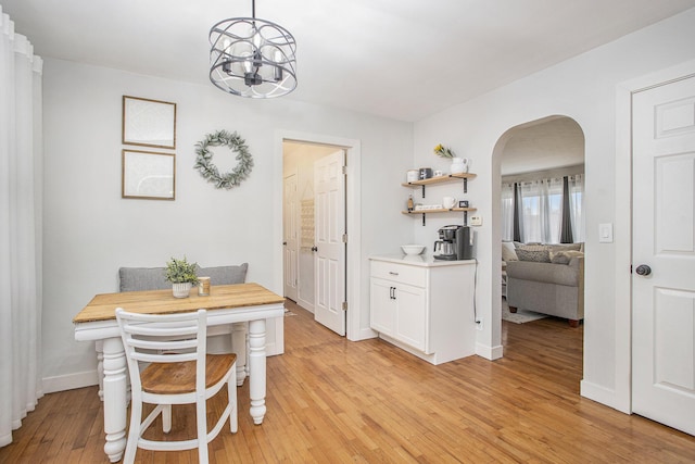 dining room with baseboards, arched walkways, an inviting chandelier, and light wood finished floors