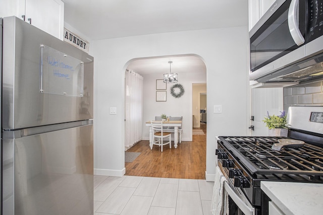 kitchen featuring light stone counters, decorative backsplash, appliances with stainless steel finishes, arched walkways, and white cabinets