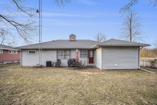 rear view of property with a patio, a lawn, a chimney, and a shingled roof