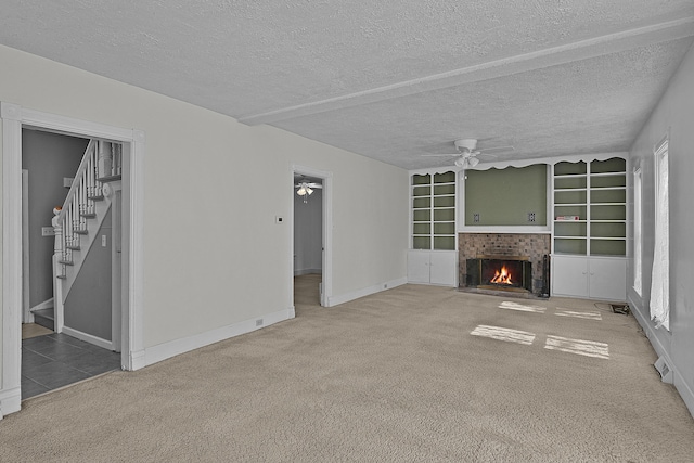 unfurnished living room with a fireplace with flush hearth, stairs, ceiling fan, and carpet floors