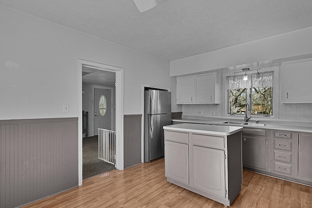 kitchen featuring light countertops, wainscoting, freestanding refrigerator, light wood-style floors, and a sink