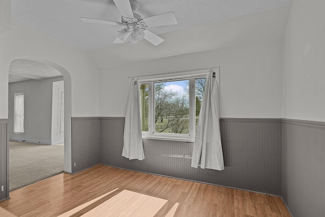 empty room with ceiling fan, wainscoting, wood finished floors, arched walkways, and a textured ceiling