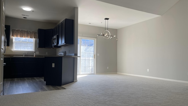 kitchen with light carpet, stainless steel microwave, a healthy amount of sunlight, and an inviting chandelier