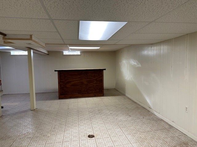 finished basement with a drop ceiling, light floors, and a bar