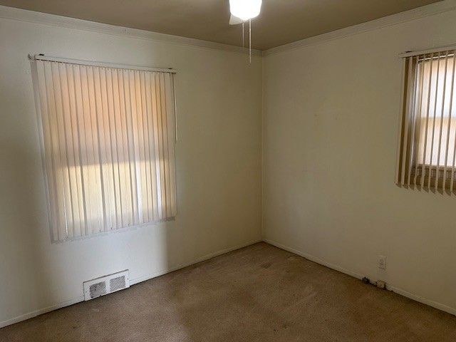 empty room with visible vents, carpet floors, and ornamental molding