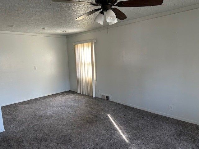 carpeted empty room featuring a textured ceiling, crown molding, visible vents, and ceiling fan