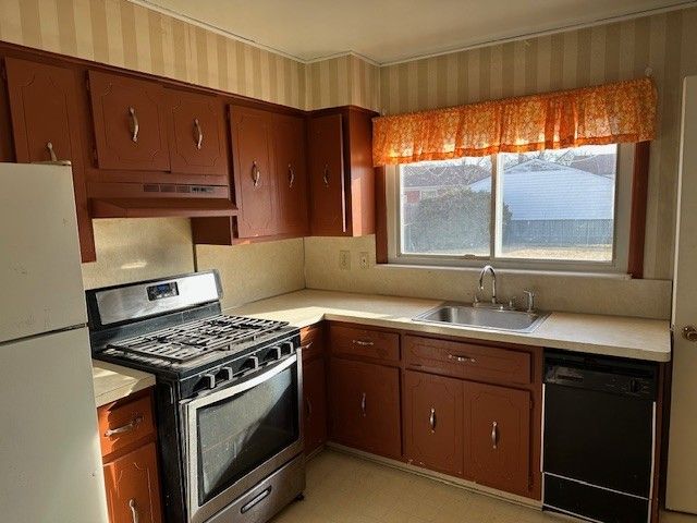 kitchen with stainless steel gas range, freestanding refrigerator, a sink, under cabinet range hood, and dishwasher