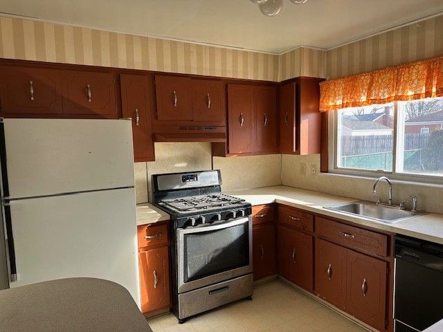 kitchen featuring stainless steel range with gas stovetop, freestanding refrigerator, a sink, black dishwasher, and under cabinet range hood