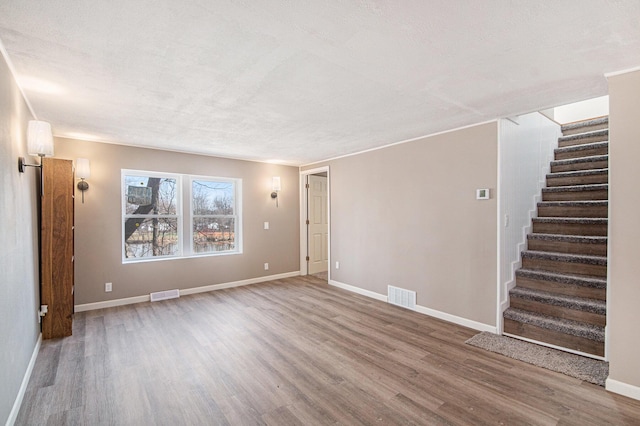 unfurnished living room featuring stairs, wood finished floors, visible vents, and baseboards