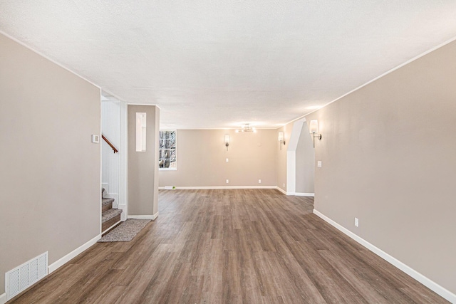 unfurnished living room with visible vents, a textured ceiling, wood finished floors, baseboards, and stairs