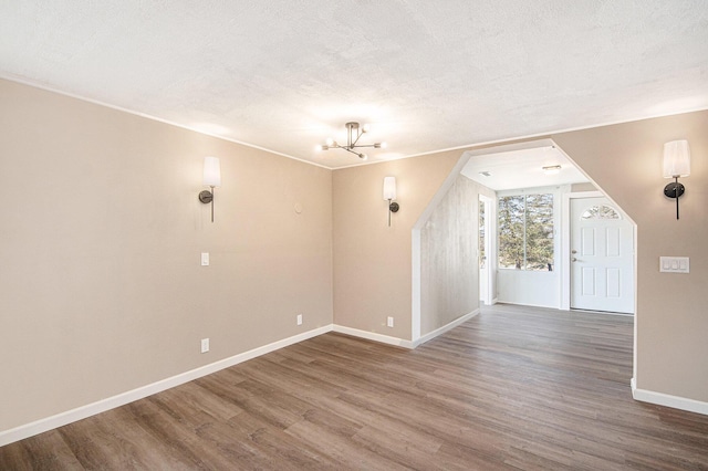 additional living space featuring baseboards, a textured ceiling, an inviting chandelier, and wood finished floors