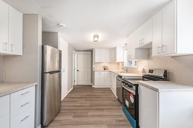 kitchen with light wood finished floors, backsplash, light countertops, appliances with stainless steel finishes, and white cabinets