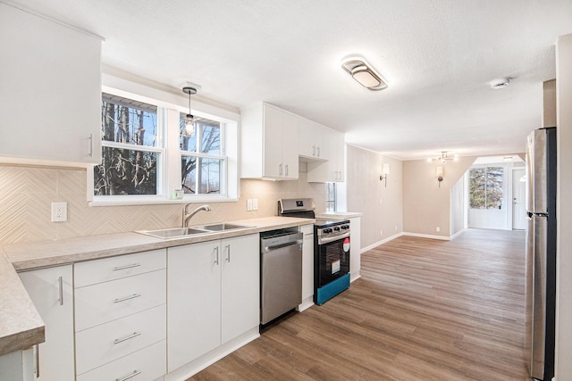 kitchen featuring wood finished floors, a sink, stainless steel appliances, white cabinets, and tasteful backsplash