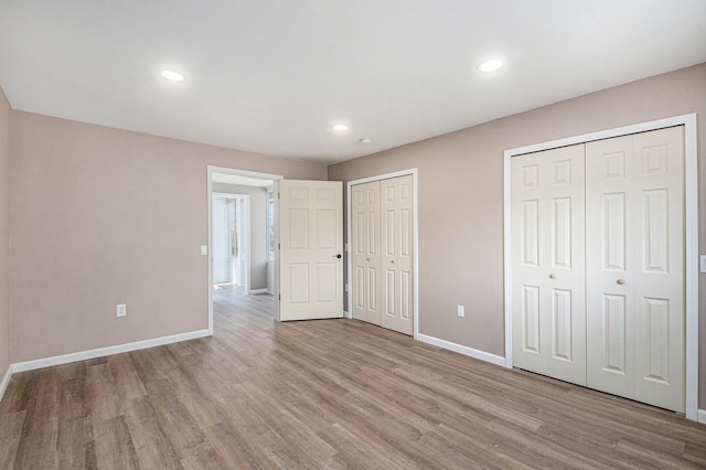 unfurnished bedroom featuring recessed lighting, baseboards, multiple closets, and light wood finished floors