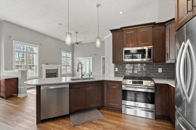 kitchen with light countertops, a tile fireplace, a peninsula, stainless steel appliances, and a sink