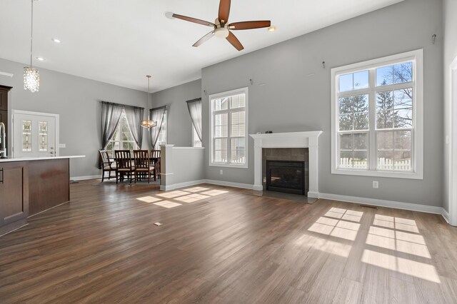 unfurnished living room with a ceiling fan, wood finished floors, baseboards, and a tile fireplace