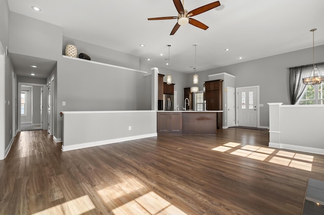 unfurnished living room with dark wood finished floors, ceiling fan with notable chandelier, baseboards, and a sink