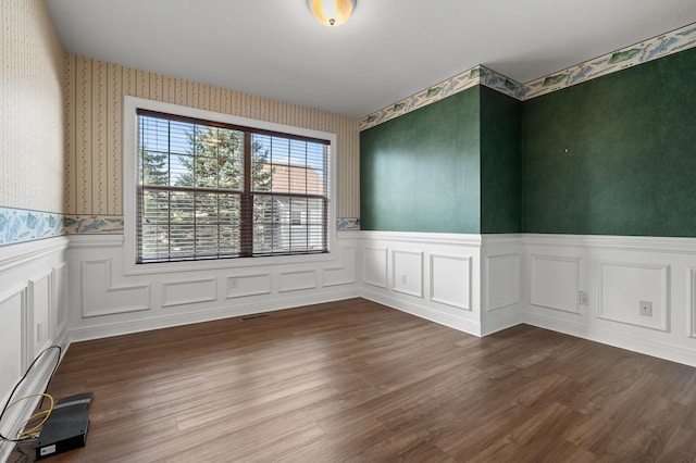 spare room featuring a wainscoted wall, wallpapered walls, and dark wood-style flooring