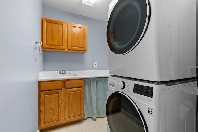 clothes washing area with cabinet space, stacked washer and clothes dryer, light floors, and a sink