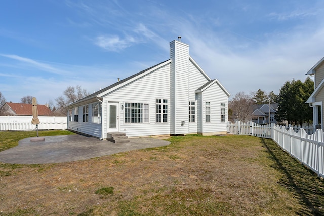 rear view of property featuring entry steps, a lawn, a chimney, a fenced backyard, and a patio area