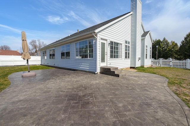 back of house featuring fence, entry steps, a lawn, a chimney, and a patio area