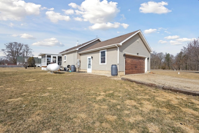 back of property featuring a yard, a garage, driveway, and a sunroom