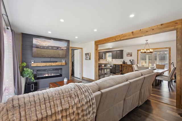 living room featuring dark wood-style floors, baseboards, recessed lighting, a glass covered fireplace, and a chandelier