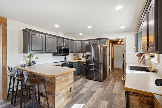 kitchen with light wood finished floors, a kitchen bar, a peninsula, stainless steel appliances, and a sink