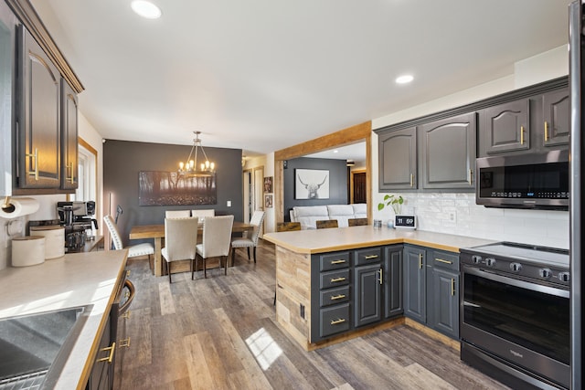 kitchen with an inviting chandelier, stainless steel appliances, light countertops, dark wood-type flooring, and tasteful backsplash