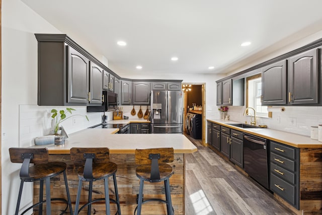 kitchen with dishwasher, a peninsula, stainless steel refrigerator with ice dispenser, wood finished floors, and a sink