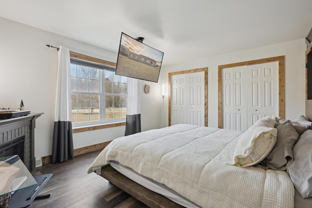 bedroom with a glass covered fireplace, baseboards, multiple closets, and wood finished floors