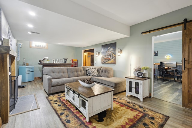 living room with a barn door, visible vents, concrete block wall, and light wood finished floors