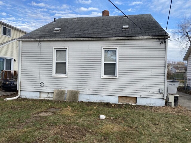 back of property featuring a chimney, a lawn, and a shingled roof