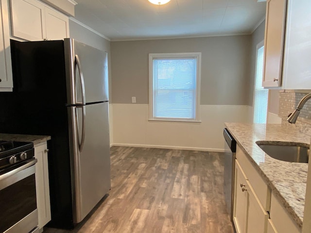 kitchen featuring light stone counters, appliances with stainless steel finishes, wood finished floors, white cabinets, and a sink