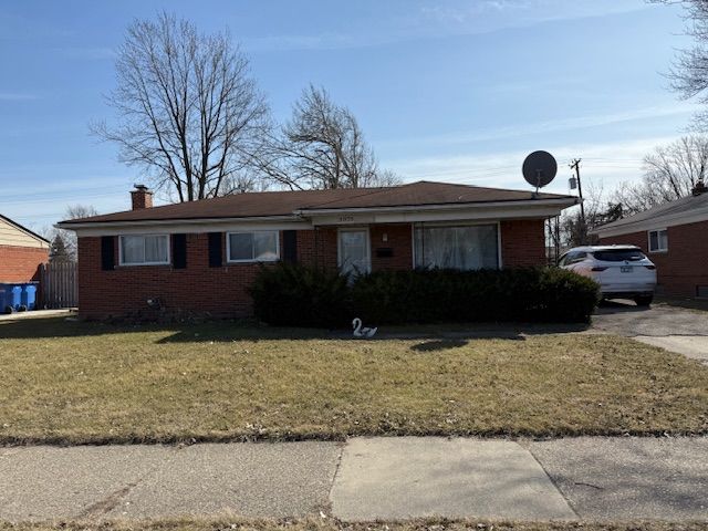 ranch-style house with brick siding, concrete driveway, a chimney, and a front yard