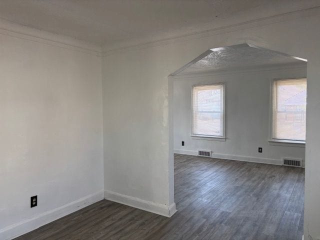 spare room with dark wood-style floors, visible vents, baseboards, and ornamental molding