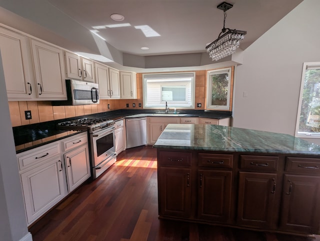 kitchen with a sink, decorative light fixtures, dark wood finished floors, appliances with stainless steel finishes, and decorative backsplash